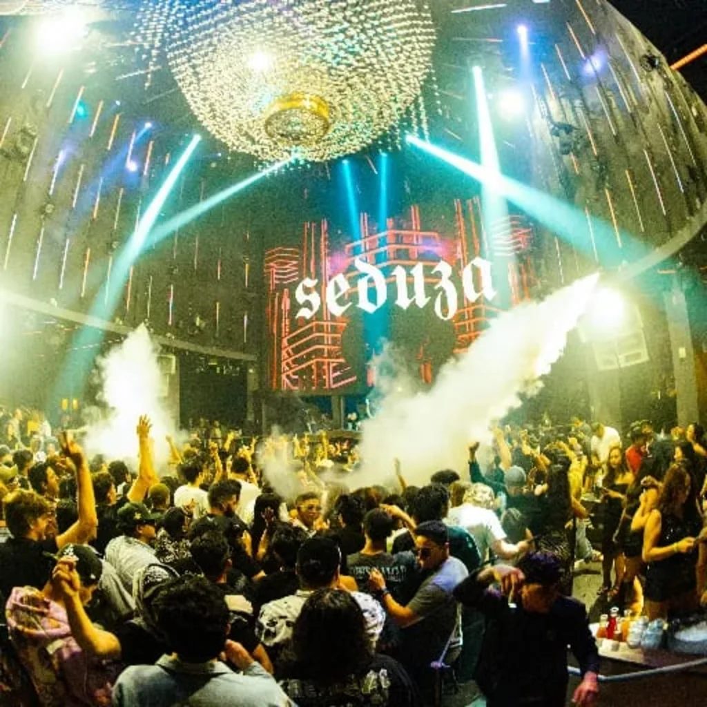 Crowd under a mirror ball with the Seduza wordmark on the LED wall and CO2 cannons firing